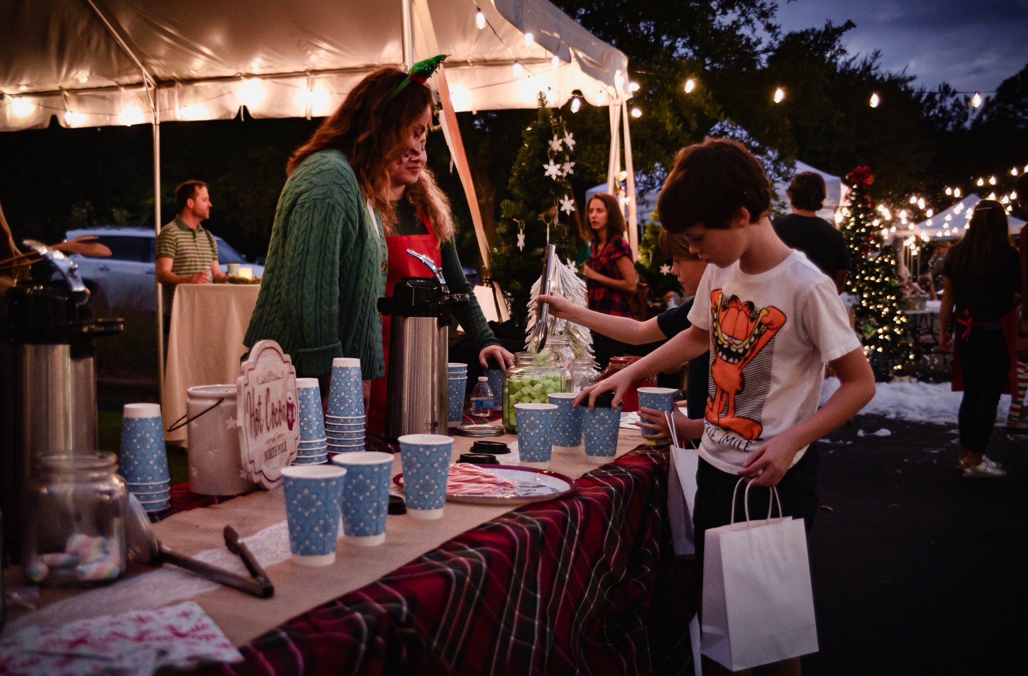 Children choosing treats at a Hot Chocolate Bar beneath Christmas string lights at a past family celebration